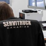 Empleada de Servitruck sentada frente a un ordenador con una chaqueta que lleva el logo de la empresa en la espalda