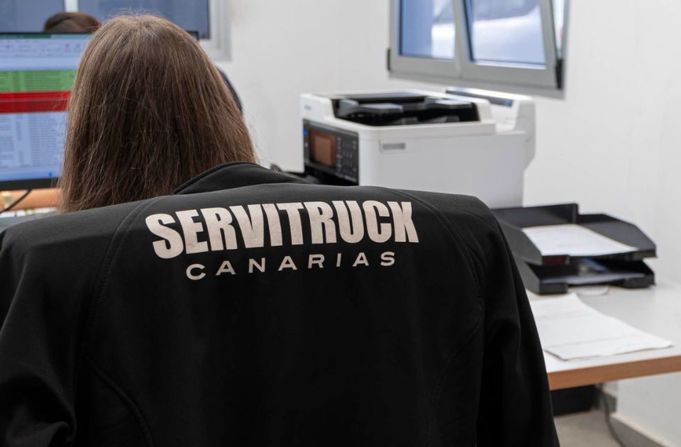 Empleada de Servitruck sentada frente a un ordenador con una chaqueta que lleva el logo de la empresa en la espalda