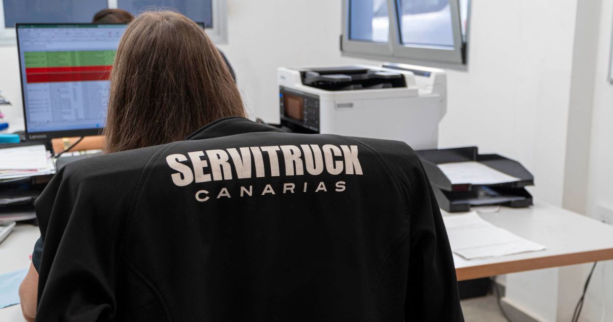 Empleada de Servitruck sentada frente a un ordenador con una chaqueta que lleva el logo de la empresa en la espalda