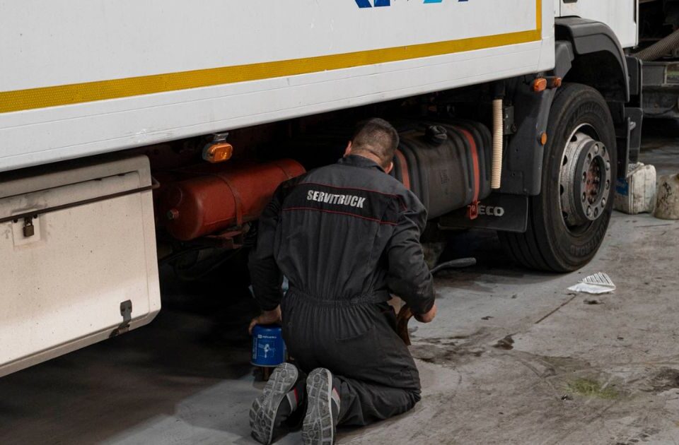 Mecánico de Servitruck arrodillado trabajando en la parte inferior de un camión sosteniendo una lata de aceite.