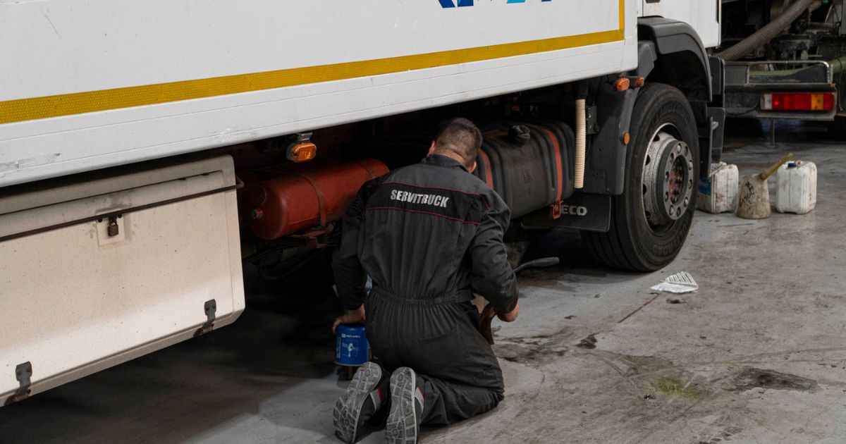 Mecánico de Servitruck arrodillado trabajando en la parte inferior de un camión sosteniendo una lata de aceite.
