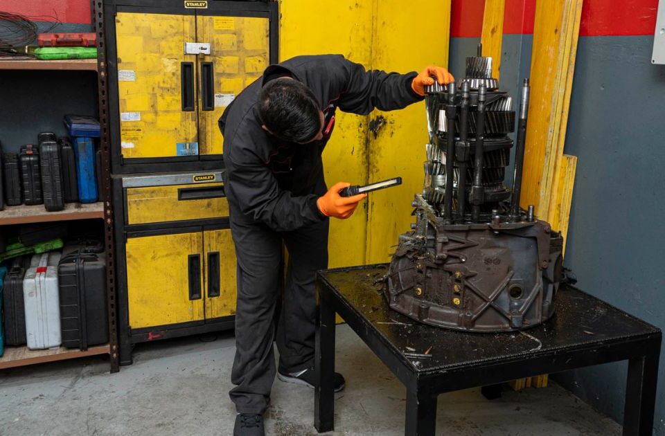 Mecánico de Servitruck trabajando en la reparación de una caja de cambios utilizando una linterna