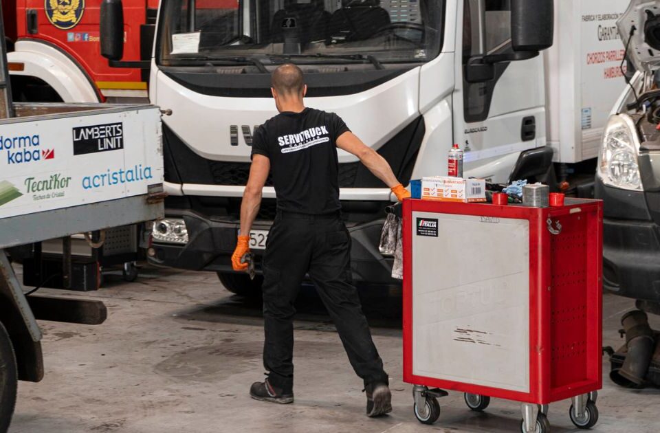 Mecánico de Servitruck trasladando un carrito de herramientas mientras trabaja en la reparación de vehículos industriales en el taller.